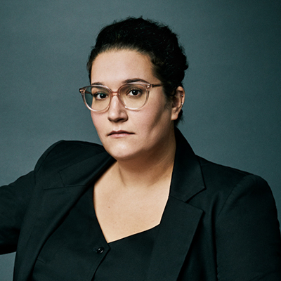 Headshot of author Carmen Maria Machado, a Latin woman wearing glasses and a black top and blazer