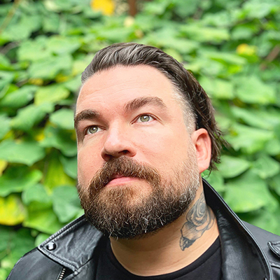 Headshot of writer Isaac Fitzgerald, a White man wearing a black leather jacket