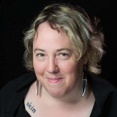 Headshot of author Kelly Link, a smiling White woman wearing knife-shaped earrings and a black top