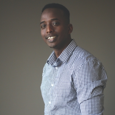 Headshot of Abdi Nor Iftin, a smiling Black man wearing a patterned button-down shirt