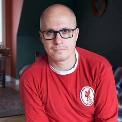 Headshot of Aleksandar Hemon, a White man with glasses wearing a red t-shirt