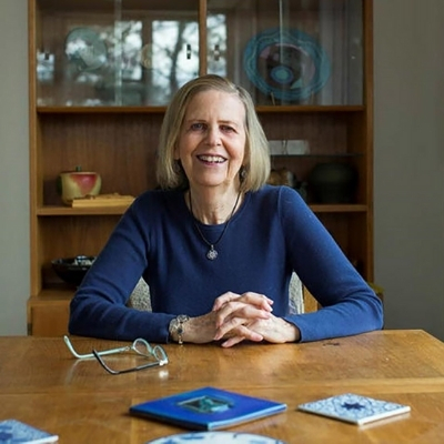 Headshot of author Bobbie Ann Mason, a smiling White woman wearing a blue long-sleeve shirt sitting at a desk