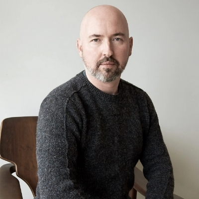 Headshot of author Douglas Stuart, a White man with a beard wearing a gray sweater