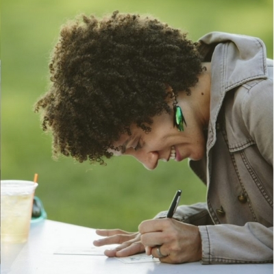Headshot of writer Ebony Flowers, a Black woman sitting at a desk and writing