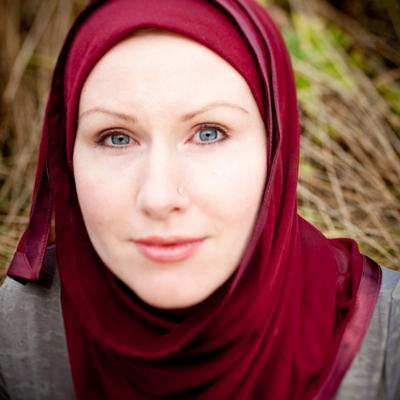 Headshot of author G. Willow Wilson, a woman wearing a red headscarf and a gray top