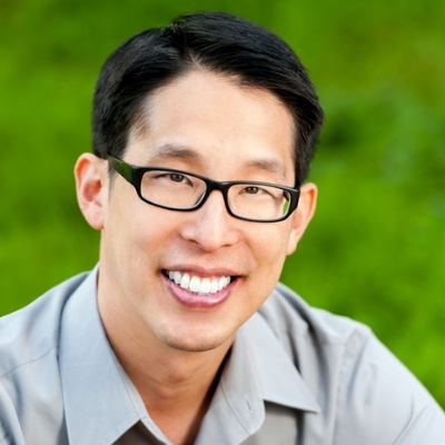 Headshot of writer Gene Luen Yang, a smiling Asian man wearing glasses and a gray collared shirt