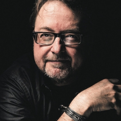 Headshot of author Luis Urrea, a Latin man with glasses and a beard wearing a black top