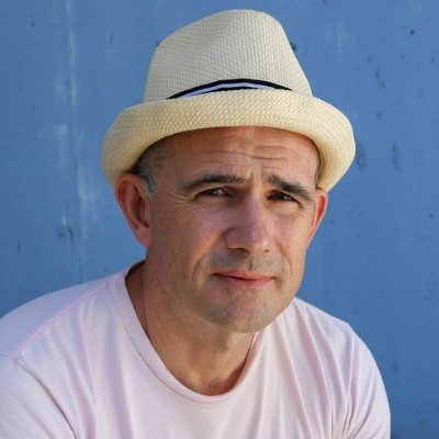 Headshot of author Mark Danielewski, a White man wearing a hat and a light t-shirt