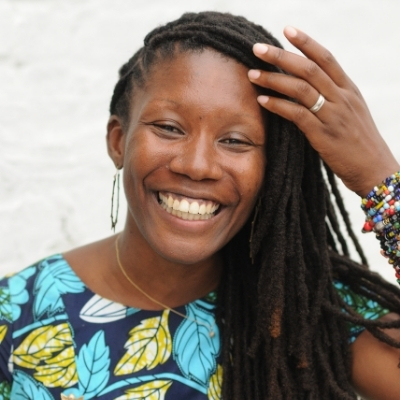Headshot of author Nicole Dennis-Benn, a smiling Black woman wearing a stack of colorful bangles and a patterned top