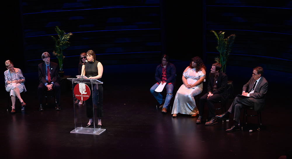 Photo of author Azareen Van der Vliet Oloomi speaking at a podium onstage surrounded by other authors
