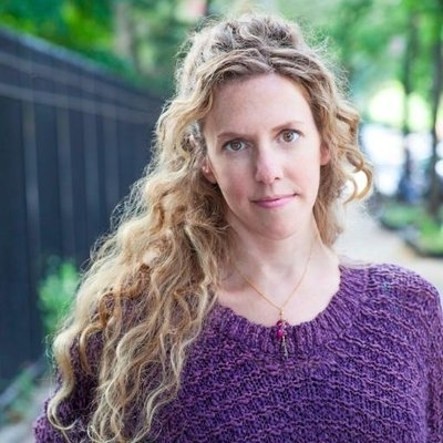 Headshot of author Robin Wasserman, a White woman with long curly hair wearing a purple sweater