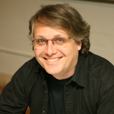 Headshot of writer Scott McCloud, a smiling White man wearing glasses and a dark collared shirt