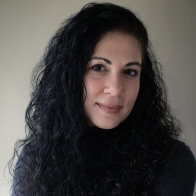 Headshot of author Susan Darraj, a smiling Arab woman with long curly hair wearing a black top