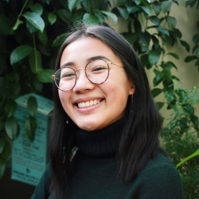 Headshot of a smiling Asian woman wearing glasses and a green turtleneck