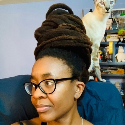 Headshot of author Nnedi Okorafor, a Black woman wearing glasses with a cat perched behind her