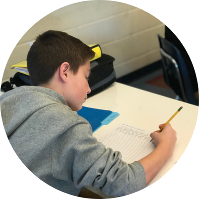 Student Writing A male student in a gray sweatshirt writing on a piece of paper in a classroom