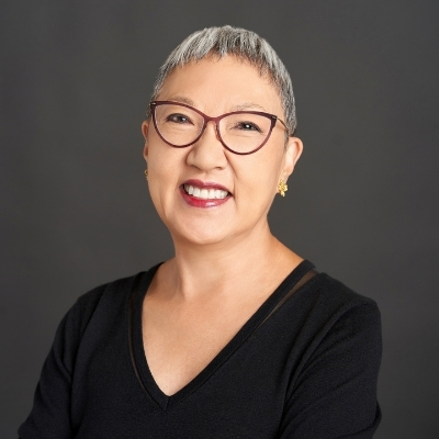 Headshot of author Eugenia Kim, an Asian woman with short white hair wearing red glasses and a black top