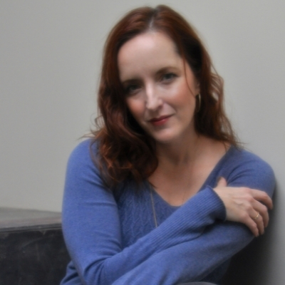 Headshot of author Rebecca Makkai, a White woman with shoulder-length red hair wearing a blue top and necklace
