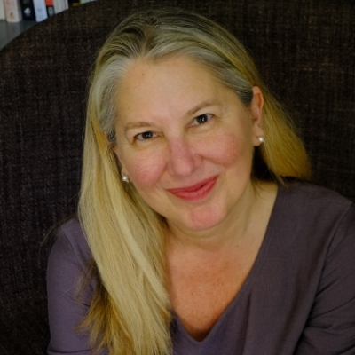 Photo of a smiling White woman with long blonde hair wearing a purple top