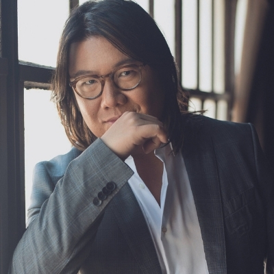 Headshot of author Kevin Kwan, a person wearing glasses, a white collared shirt, and a gray suit jacket