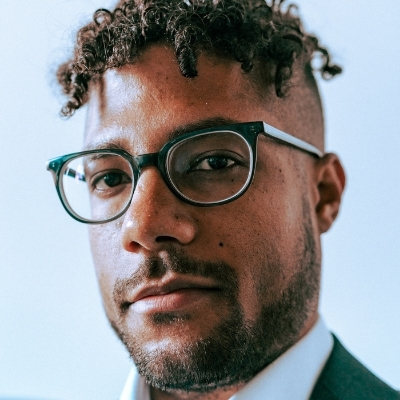 Headshot of author Mateo Askaripour, a person wearing glasses and a suit