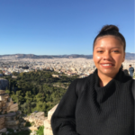 Headshot of Literary Education Programs Assistant Maya Lawrence, a Black woman smiling at the camera wearing her dark hair in a bun and a black sweater top