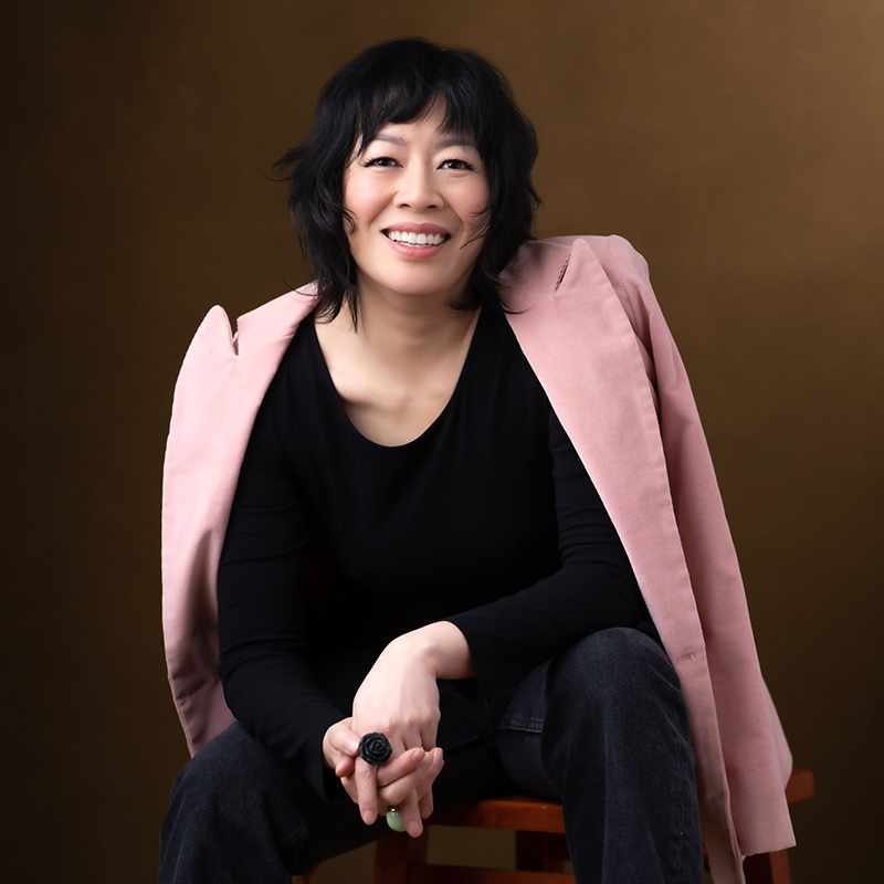 Headshot of Lauren Francis-Sharma, a smiling Black woman wearing glasses, a patterned scarf, and a white top