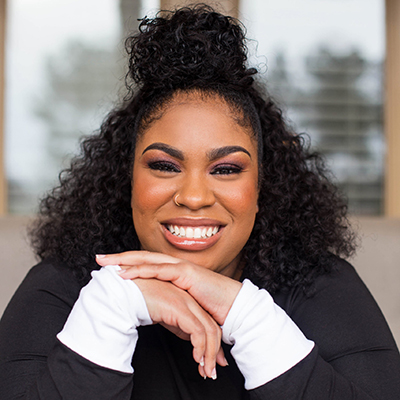 Headshot of author Angie Thomas, a smiling Black woman with a top knot wearing a black top