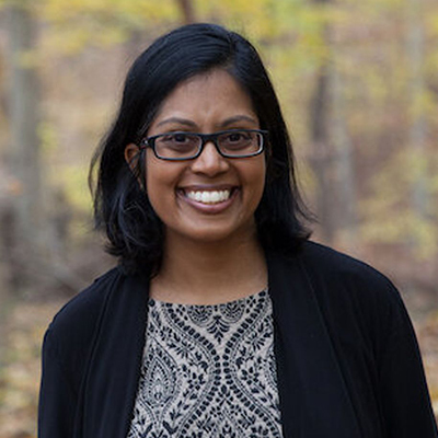 Headshot of author Mathangi Subramanian, a smiling South Asian woman wearing glasses and a black sweater