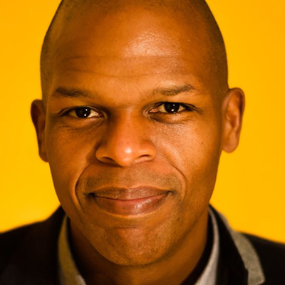 Headshot of author Maurice Carlos Ruffin, a smiling Black man against a yellow background