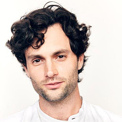 Headshot of actor Penn Badgley, a White man with dark curly hair wearing a white top