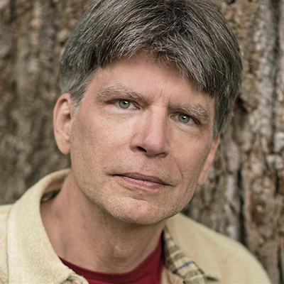 Headshot of author Richard Powers, a White man wearing a light collared top