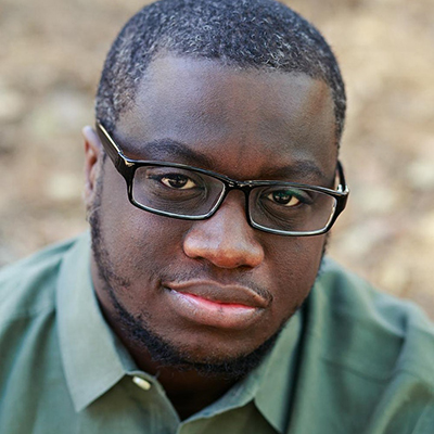 Headshot of author Rion Amilcar Scott, a Black man with glasses and a green collared top