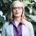 Headshot of Lacey Dunham, a White woman wearing glasses, a purple collared top, and a gray blazer